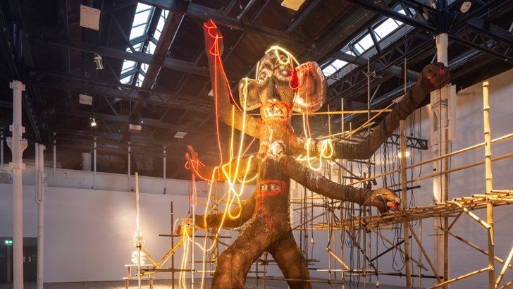 A large multi-limbed figure draped in neon, in Tramway's vast main gallery