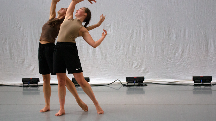 Two dancers strike an identical arched pose in front of a white backdrop