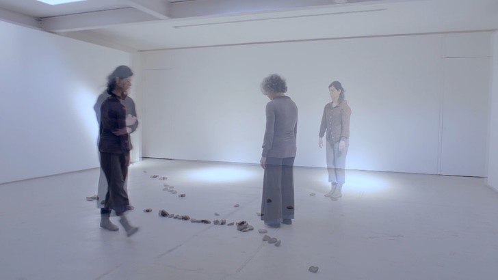 Three figures appear slightly transparent in a dark studio