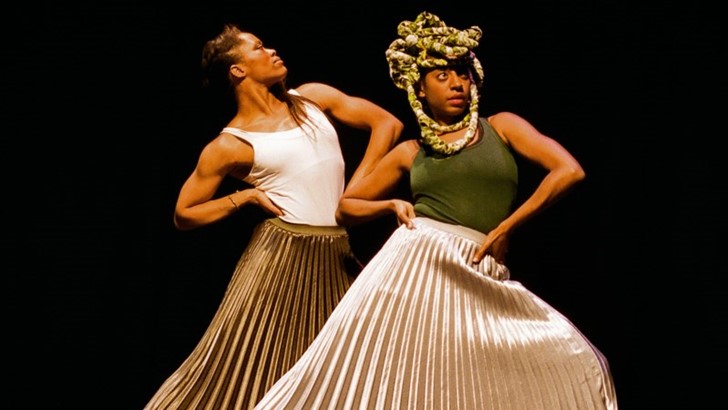 Two performers in pleated metallic skirts strike a powerful pose