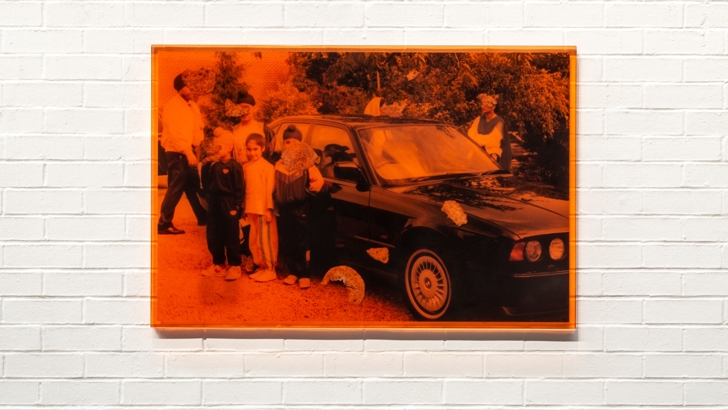 A red-tinted family photo hangs on a white gallery wall