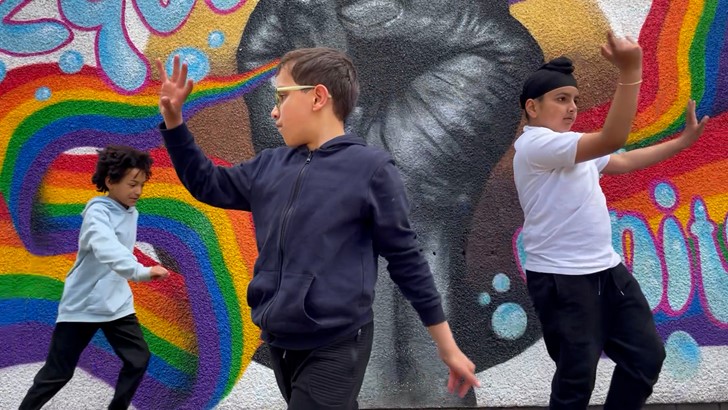 A group of children dance in front of a colourful mural