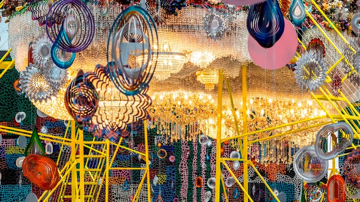 A packed and colourful installations includes countless hanging sculptures, and a raised metal platform holding a cloud-like light sculpture