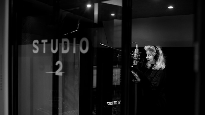 A woman stands in a recording booth of a studio