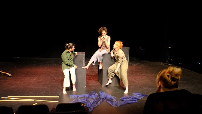 Three performers sit on black plinths of different heights