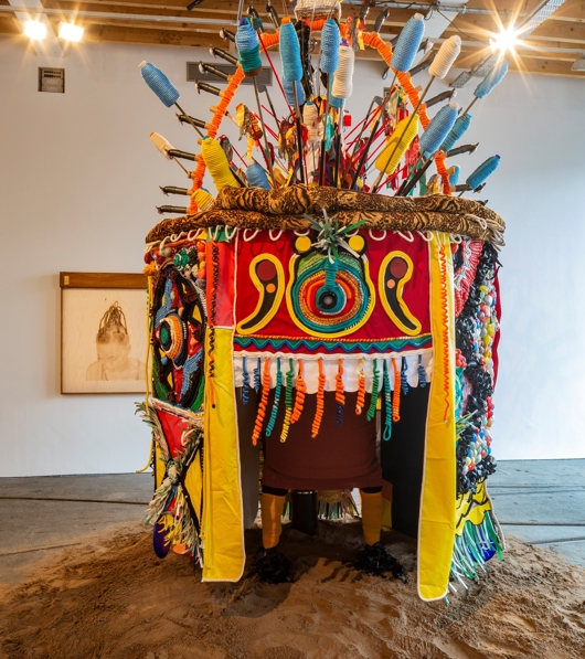 A colourful embroidered tent-like structure sits in a white washed gallery