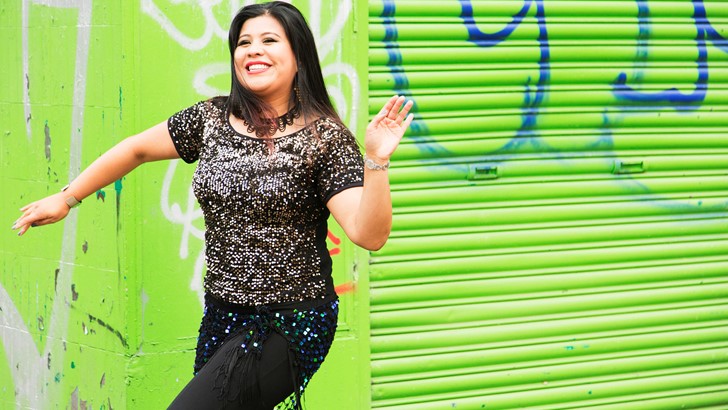 A woman strikes a dance pose in front of bright green shop shutters
