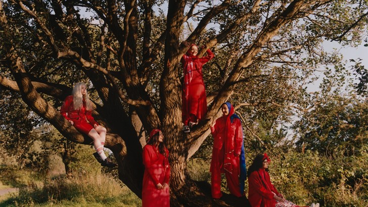 Several women, dressed in red, are seated and standing in and around a large tree