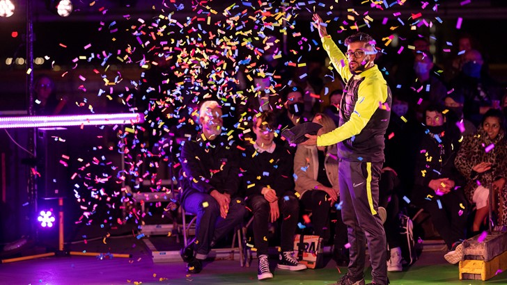 A man in a tracksuit looks on as confetti flutters around him. There is a seated audience in the background.
