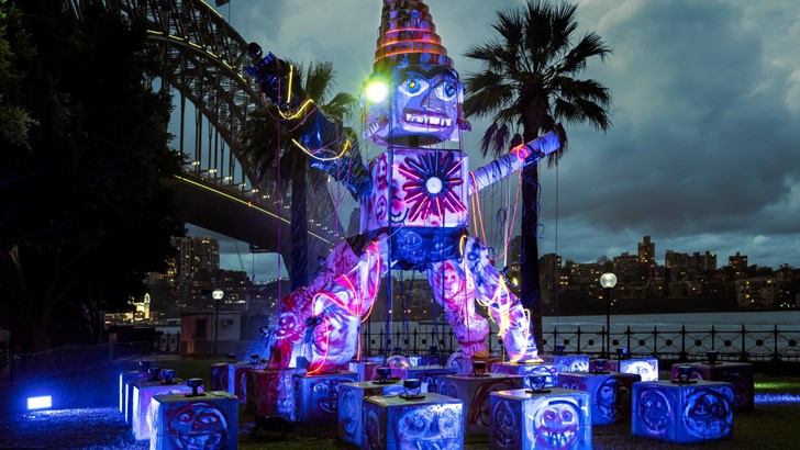 A huge humanoid sculpture dominates a nighttime cityscape