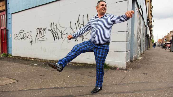 A man strikes a dance pose against a graffitied wall