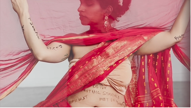 A woman poses in a red sari, her arms and stomach scrawled with words