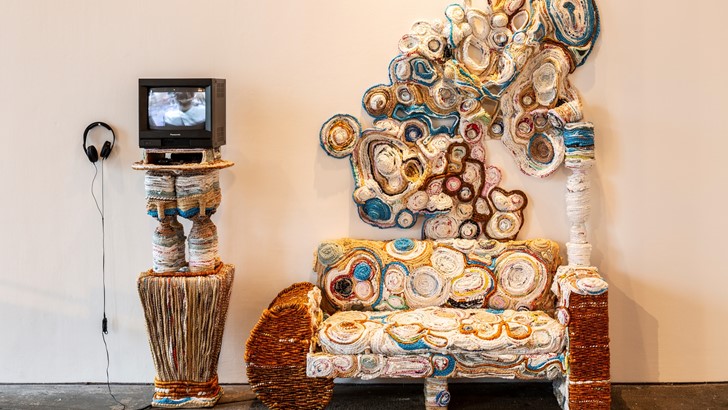 An intricately woven installation featuring a bench-like structure and a television monitor