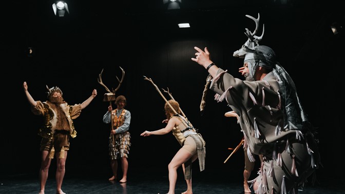 Four performers pose on a darkened stage, their costumes feature antlers