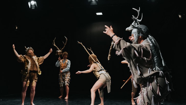 Four performers pose on a darkened stage, their costumes feature antlers