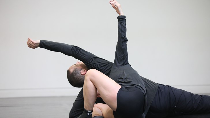 A male and female dancer in an interwined pose, arms outstretched 