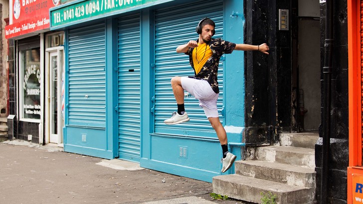 A man strikes a dance pose in front of bright blue shop shutters