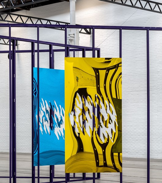 Metal sculptures are displayed on a cage-like steel structure in a large gallery