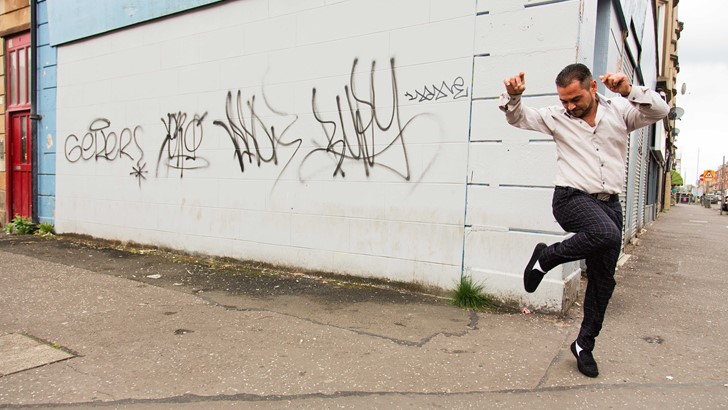 A man strikes a dance pose against a graffitied wall