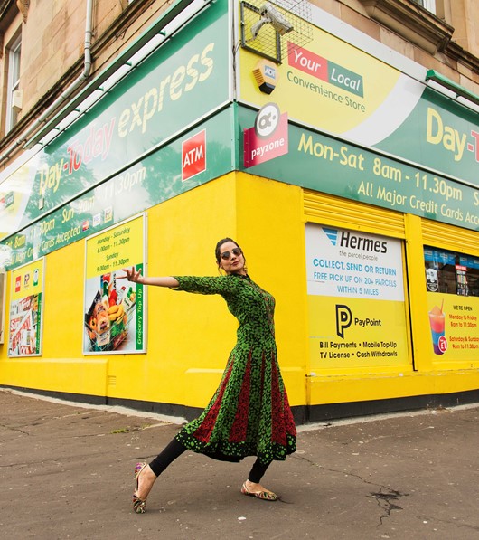 A woman in traditional costume poses in front of a brightly coloured shopfront