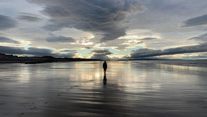 A lone figure is silhouetted in a vast sunset seascape