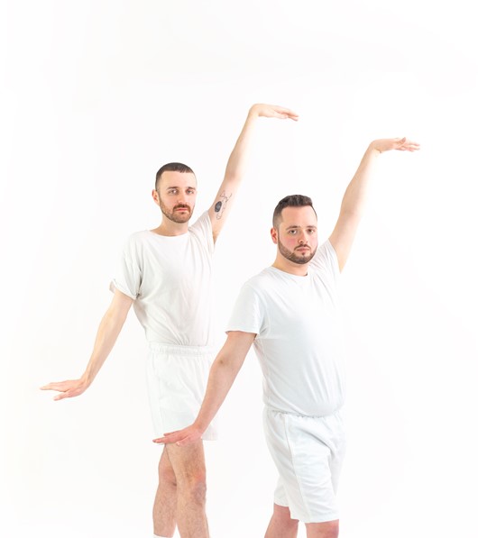 Two men in matching matching sports outfits strike an identical pose, right arms raised