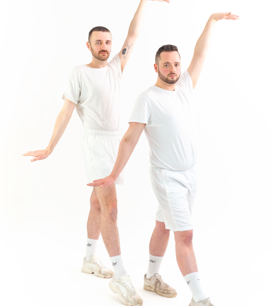 Two men in matching matching sports outfits strike an identical pose, right arms raised