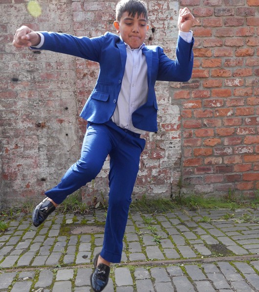 A young performer jumps in a dance move, a brick wall behind them