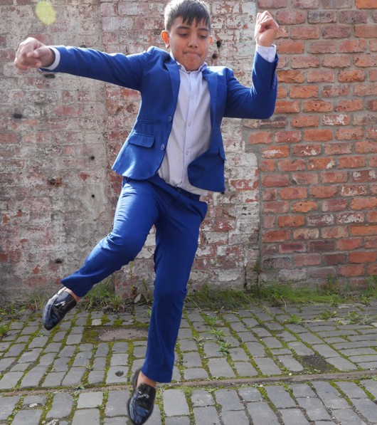 A young performer jumps in a dance move, a brick wall behind them