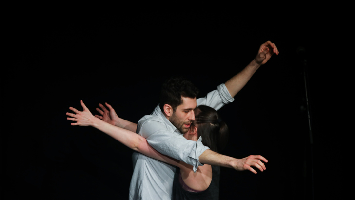 Two performers dance together on a darkened stage