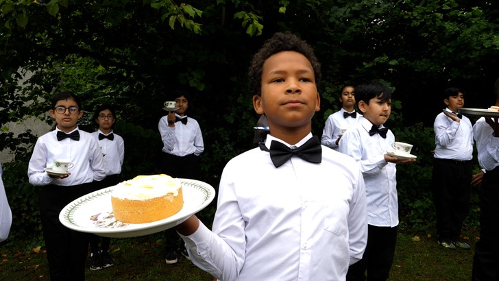 Children are pictured in shirts and bow ties, the central figure holding a cake on a plate