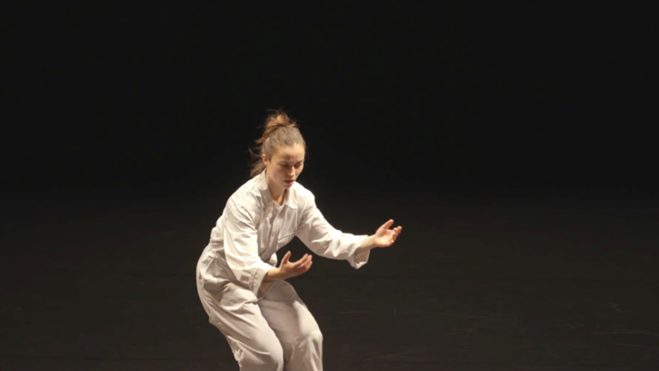 Penny Chivas performs in a white boiler suit, against a dark background