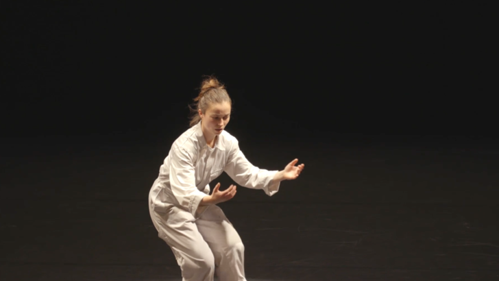 Penny Chivas performs in a white boiler suit, against a dark background