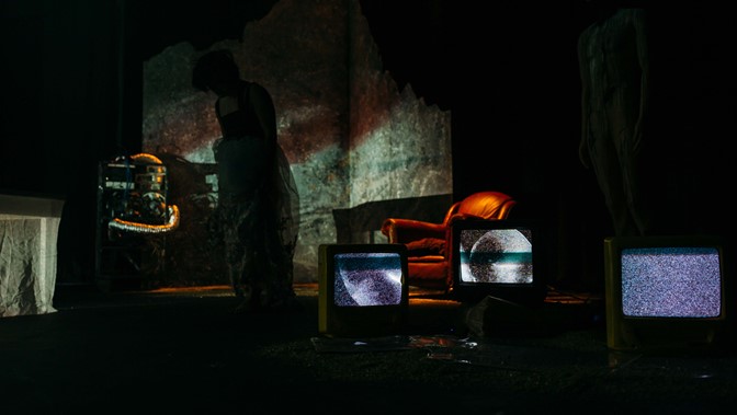 A dimly lit installation including a leather armchair and three television screens displaying static