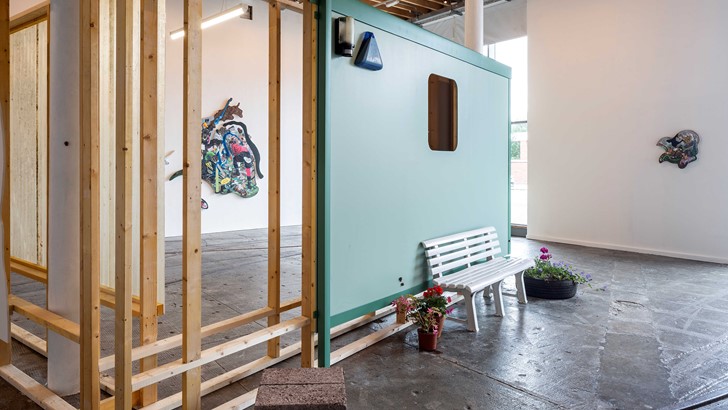 A gallery installation including irregularly shaped paintings, wooden boards and a garden bench