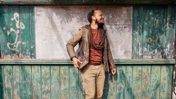 The artist Amartey Golding poses against a weathered wooden building 