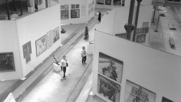 A black and white photo of people in a large gallery space, taken from above